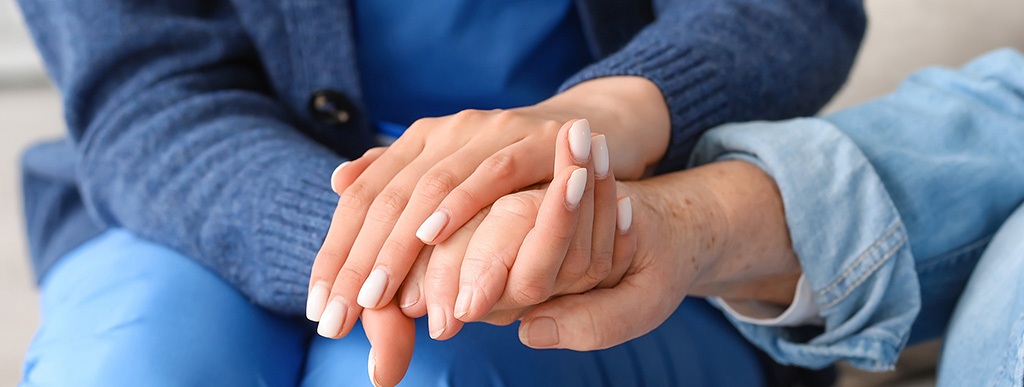 Caregiver holding elderly patients hands, comforting.